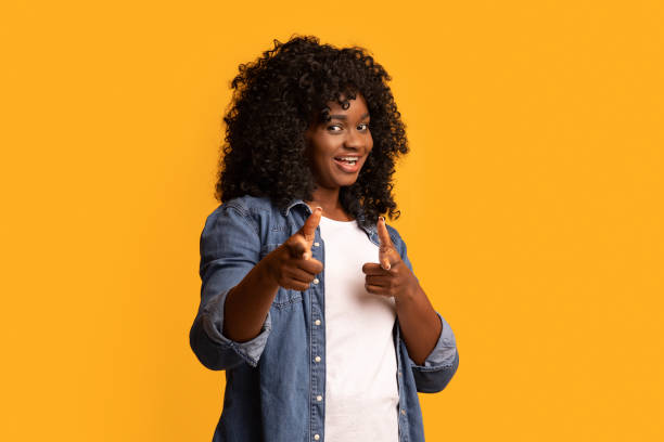 istock Cheerful black woman indicating at camera on yellow 1305456362