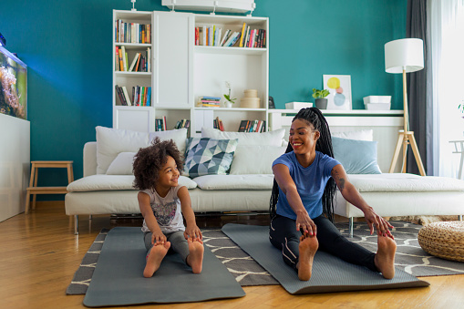African woman and her daughter sitting on exercise mat an stretching after exercises.
