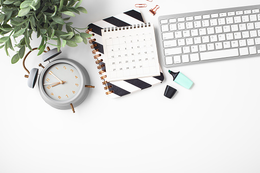 Alarm clock and calendar on white office table, flat lay