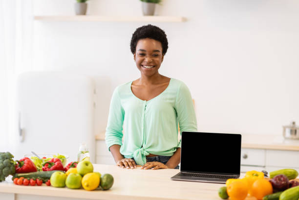 istock Black Female Standing Near Laptop With Blank Screen In Kitchen 1305457912