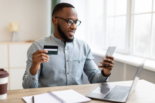 istock African Man Using Credit Card And Phone Sitting In Office 1305458159