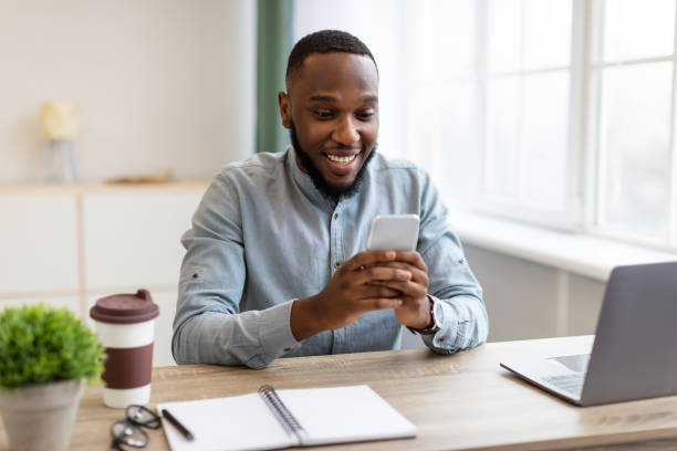 istock Happy African Businessman Using Phone App Sitting At Workplace Indoors 1305458202
