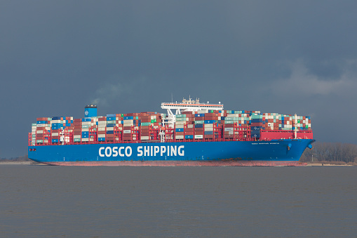 Stade, Germany - January 26, 2021: Fully loaded container ship COSCO SHIPPING SCORPIO on Elbe river heading to Hamburg