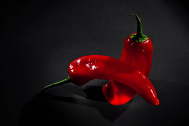 istock Red peppers close up. Vegetables on a black background. Contrasting dramatic light as an artistic effect. The concept of sex and sexual intercourse. 1305460246