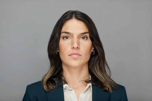 Studio portrait of a young woman shot against a plain background.
Made in Barcelona.
Spanish model.
Businesswoman headshot studio portrait looking at the camera.