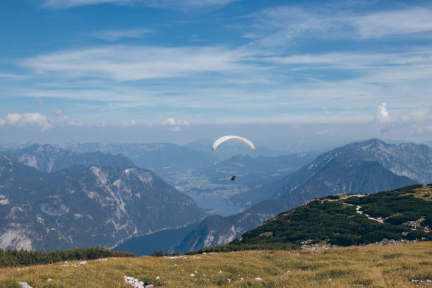 istock athlete with white-and-yellow parachute hovers over Mount Krippenstein in upper Austria, enjoying view of valley and rest of the Austrian alps. Ideal sunny weather without gusty winds for paragliding 1305463835