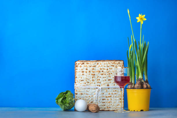 Jewish holiday Passover concept with wine, matzah, menorah and yellow daffodil on a blue background
