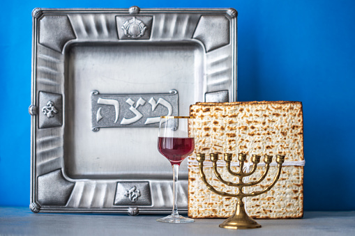 Jewish holiday Passover concept with wine, matzah, menorah and seder plate on a blue background