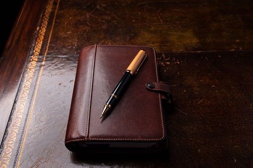 Brown leather diary and pen on an old desk.