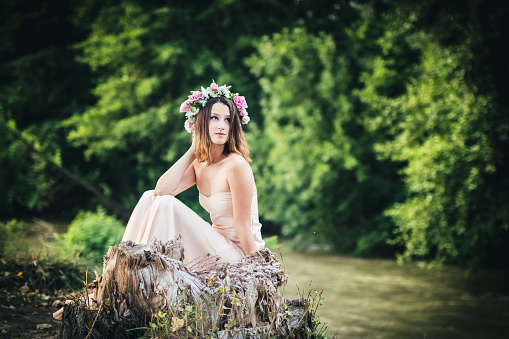 Young brunette beauty with floral wreath on her head in nature.