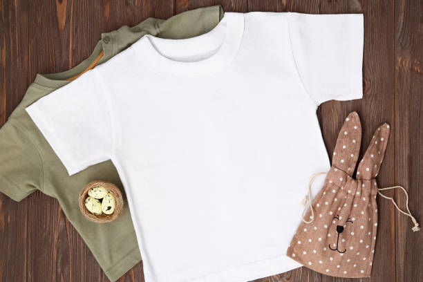 istock Two t-shirt green and white. Mockup with Easter eggs, nest and bunny candy bag flat lay on brown wooden background, template 1305479057