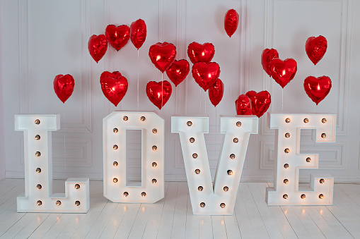 Love big letters with led retro bulbs glowing. Word LOVE illuminated with a big letters. Inscription is love. Glowing large letters. Wedding decor. Red heart balloons. air balls in shape of red heart
