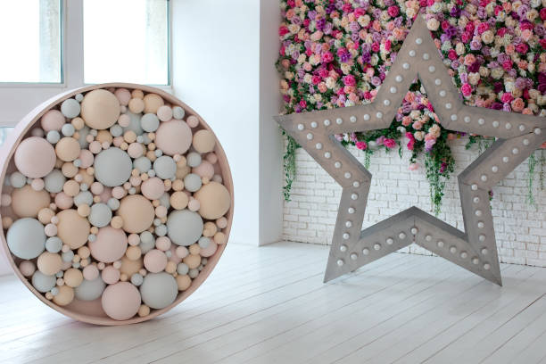 Decorative star with led retro lamp bulbs glowing. Big star with bulbs near wall with flowers. Star shaped white LED lights lamp. Wedding decoration. Decorated brick wall with Colorful balls. Holiday estrella decorativa con bombillas retro led brillantes. gran estrella con bombillas cerca de la pared con flores. lámpara de luces led blancas en forma de estrella. decoración de bodas. pared de ladrillo decorada con bolas de colores. día festivo