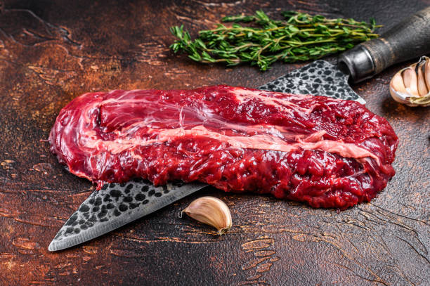 Raw organic machete or skirt steak on a butcher knife . Dark background. Top view