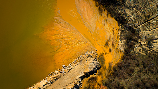 Gravel and sand open pit mining, pond with yellowish sediments - aerial view