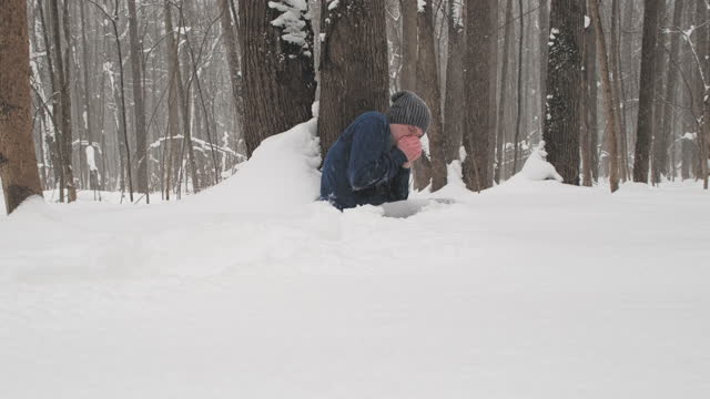 Drunk man without a jacket freezes in the forest sitting on snow near a tree