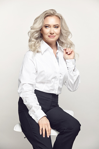 Stylish aged woman wearing in fashionable white casuals gently and dreamily looking away, has a beautiful clean skin and curly blonde hair.