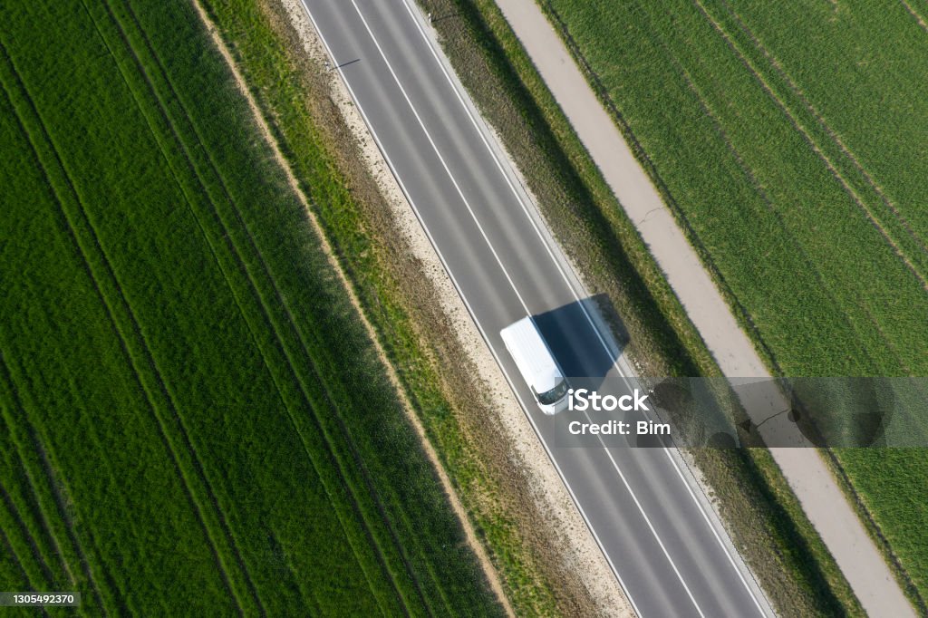White Delivery Van on the Road from Above Aerial view of a white delivery van speeding on the road between green fields in spring. Van - Vehicle Stock Photo