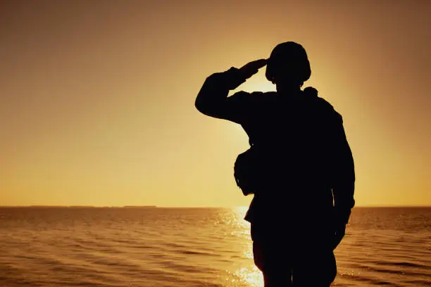 Photo of Silhouette of soldier salutes on sunset background