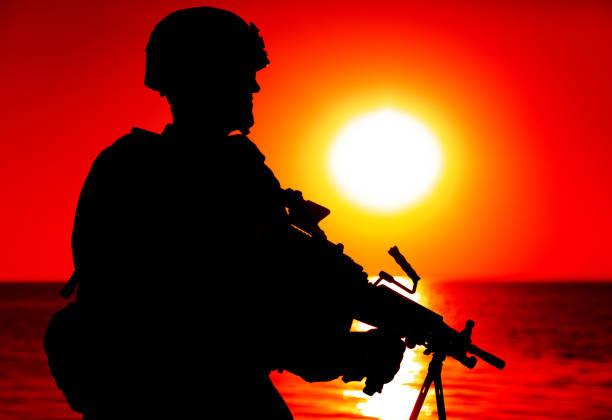 istock Silhouette of soldier with machine gun on shore 1305492544