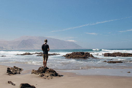 A male man standing on the shore of a beautiful sand beach in Iquique. Man experiencing the beauty of nature