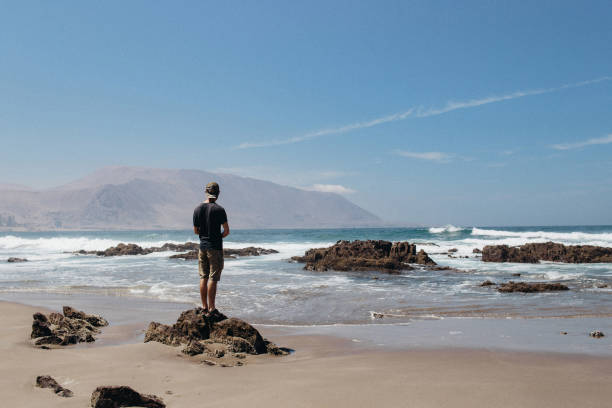 Man looking at beautiful ocean view A male man standing on the shore of a beautiful sand beach in Iquique. Man experiencing the beauty of nature chile tourist stock pictures, royalty-free photos & images