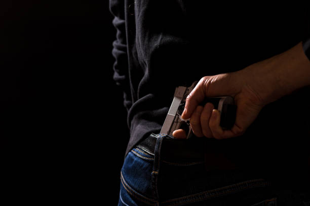 The man hides the gun behind his back. Prepare weapons, Permit to carry weapons. Free sale of weapons Man hides his gun behind his back, on a black background. gunman photos stock pictures, royalty-free photos & images
