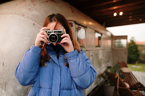 A young woman with a vintage camera by a restored american camper trailer