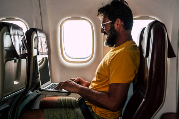 istock Hipster man with beard work on laptop computer sitting on board on airplane flight during travel - concept of free office remote worker and smart working lifestyle - people use connection technology inside fly aircraft 1305498140