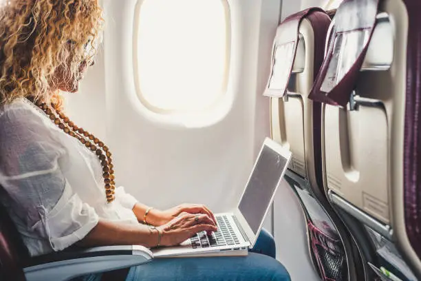 Modern young businesswoman work on flight travel airplane on board with wireless connection - people use technology laptop computer in travel - concept of remote workers and smart working free office lifestyle
