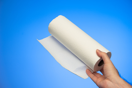 Kitchen paper roll wipes held in hand by Caucasian male hand studio shot isolated on blue background.