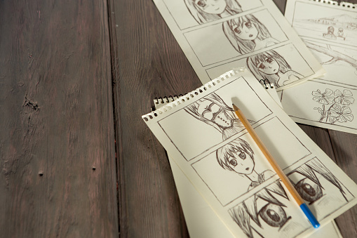 Artist drawing an anime comic book in a studio. Wooden desk, natural light