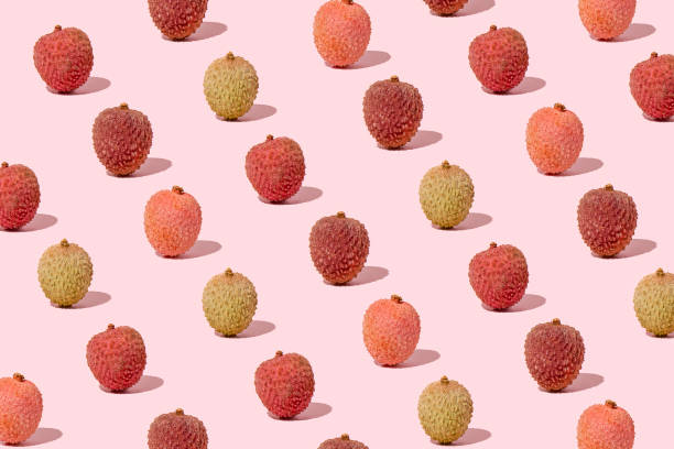 Creative pattern made with fresh colorful lychees against pastel pink background. Minimal summer fruit layout.