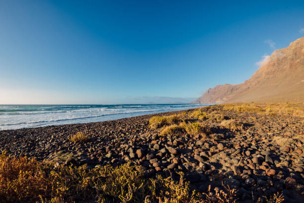 Famara beach with scenic landscape, ocean and mountains in Lanzarote, Canary islands Famara beach with scenic landscape, ocean and mountains in Lanzarote, Canary islands caleta de famara lanzarote stock pictures, royalty-free photos & images