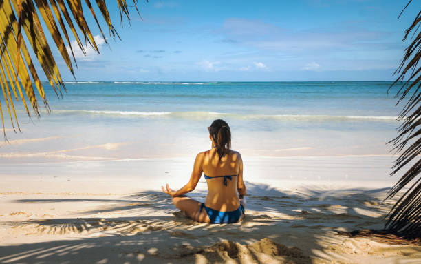 istock Young woman meditating on beach 1305508758