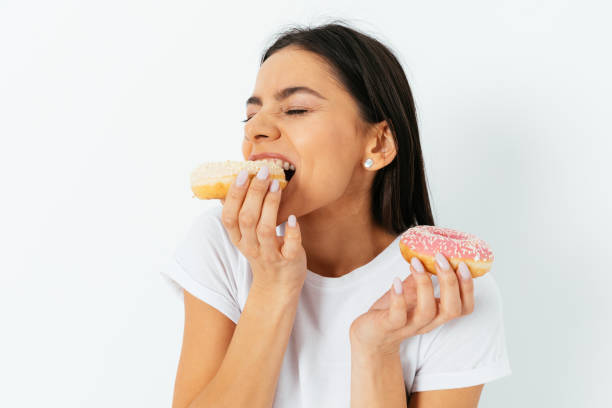 portret pięknej młodej brunetki gryzącej pączki - donut glazed bakery unhealthy eating zdjęcia i obrazy z banku zdjęć