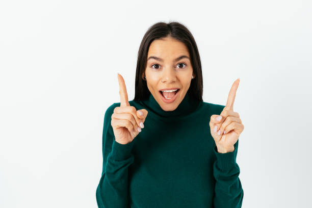 istock Brunette woman pointing with two hands up and looking at camera 1305512776