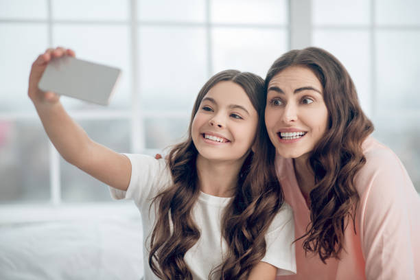 istock Long haired adorable mom and daughter taking selfie 1305514301