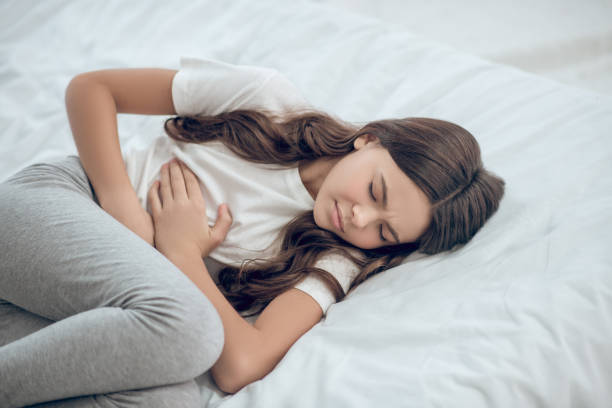 Unhappy teenage girl lying holding belly with hands stock photo
