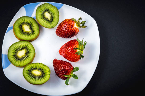 istock Sliced kiwis and strawberries on a white plate with a black background 1305515665
