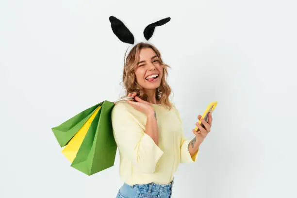 Photo of Easter shopping, funny young woman wearing toy bunny ears holding paper bags