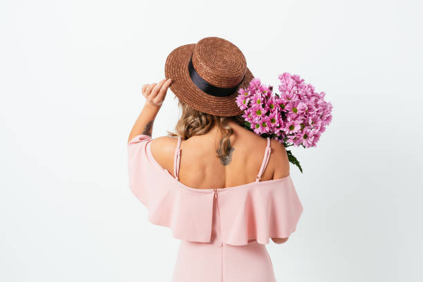 Rear view young woman with bouquet of flowers Rear view young woman with bouquet of flowers wearing pink dress and straw hat, standing on white studio background. back shoulder tattoos for women pictures stock pictures, royalty-free photos & images