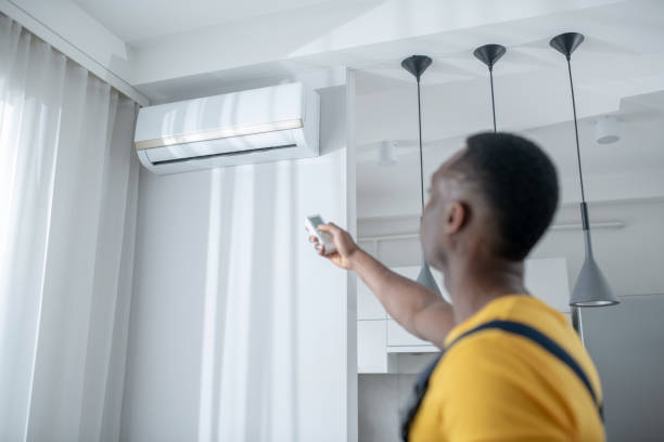 istock Dark-skinned service man in yellow tshirt installing the air-conditioner 1305517053