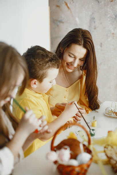 istock Mom teaches children to draw Easter eggs at table in yellow clothes 1305520231