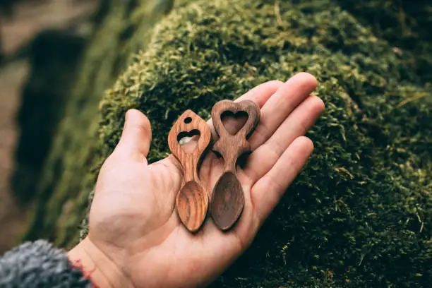 Wooden love spoons from Wales in hand on mossy stone background. Traditional welsh wooden spoons. Handcrafts.