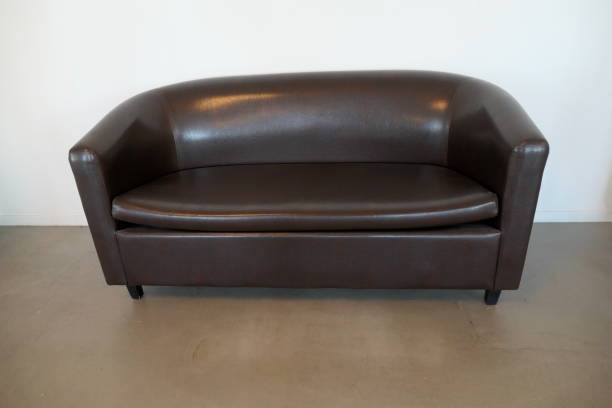istock Leather sofa, brown, on beige-brown floor in front of a white wall. 1305522002