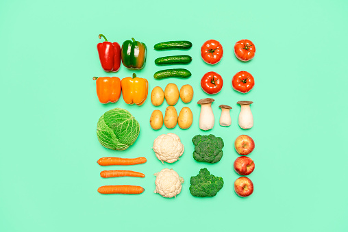 Creative layout with fresh vegetables and fruits, isolated on a green background. Flat lay with healthy food aligned on a tabletop. Vegan groceries.