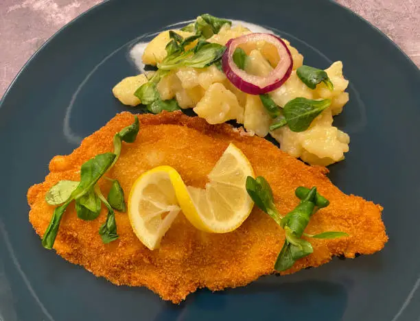 Golden breaded plaice fish fillet with potato salad and lemon.
