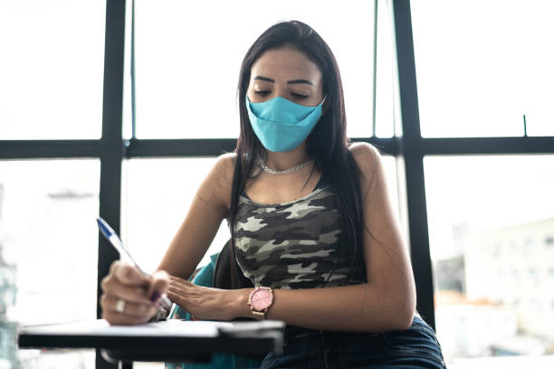 istock Female student taking notes or taking a test in a university - wearing face mask 1305525447