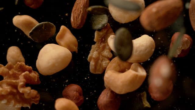 SLO MO LD Nuts and seeds mix falling onto a black surface